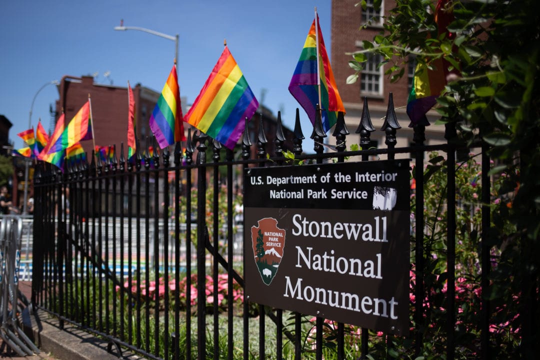 stonewall national monument sign on a fence with rainbow flags